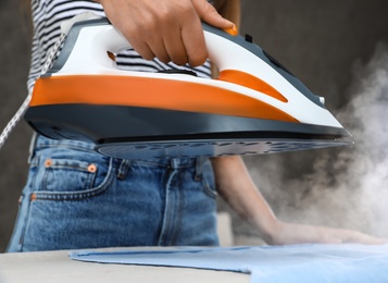 Photo of Young woman ironing clothes on board at home, closeup