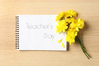 Notebook with words TEACHER'S DAY and beautiful yellow flowers on wooden table, flat lay