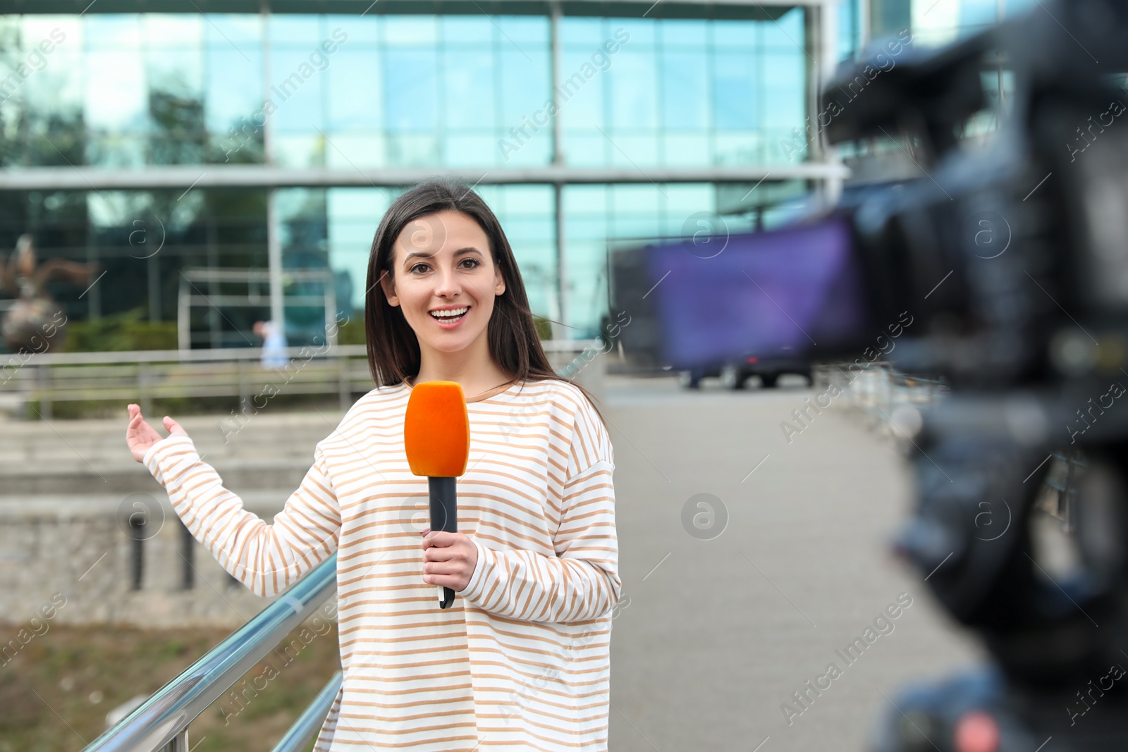 Photo of Young female journalist with microphone working on city street