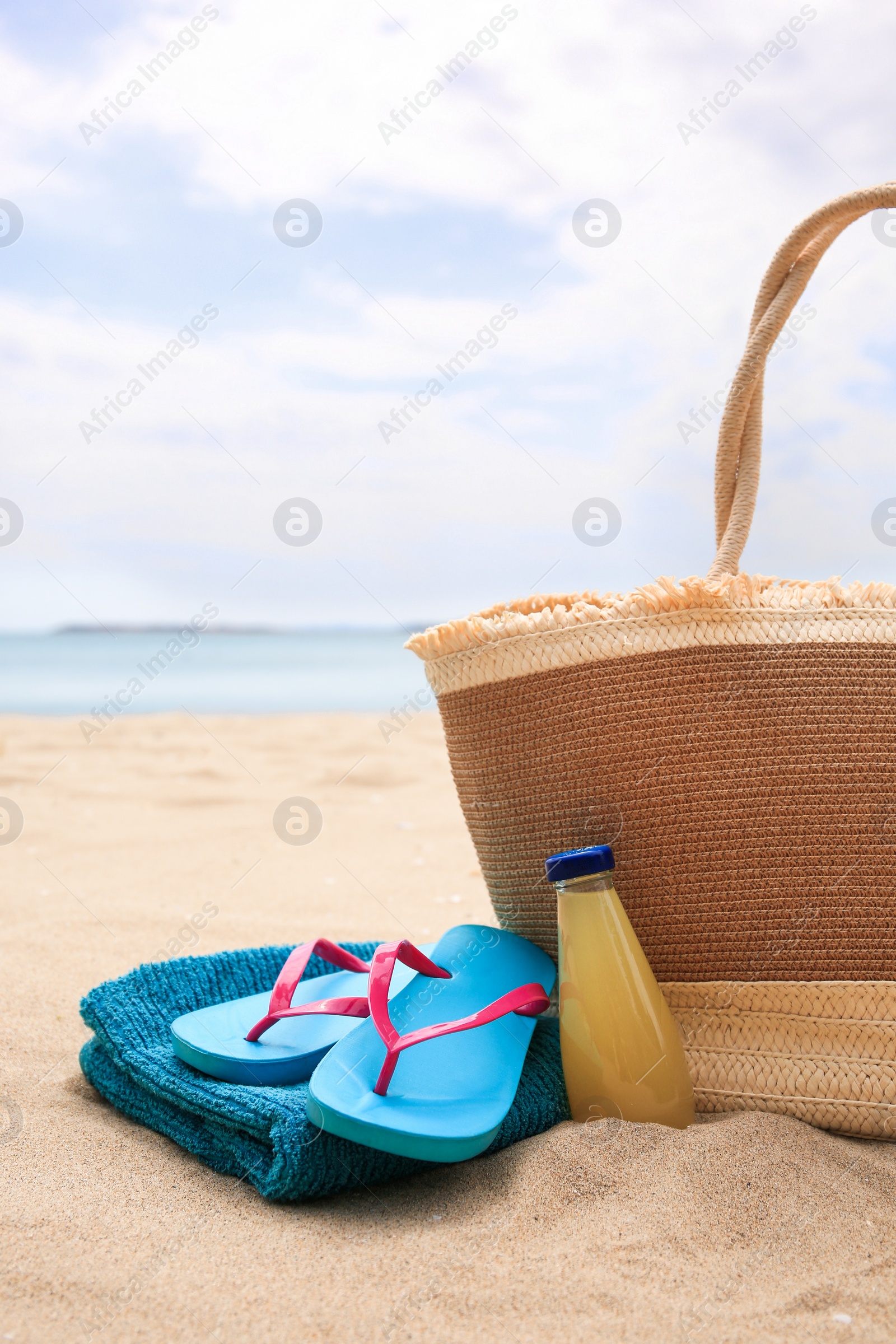 Photo of Straw bag, flip flops, towel and bottle of refreshing drink on beach
