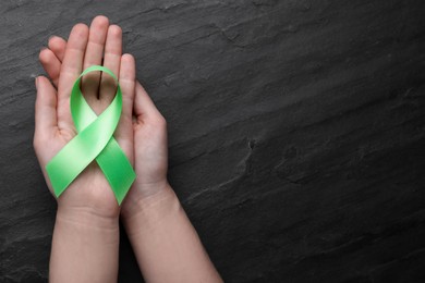 Photo of World Mental Health Day. Woman holding green ribbon on black background, top view with space for text