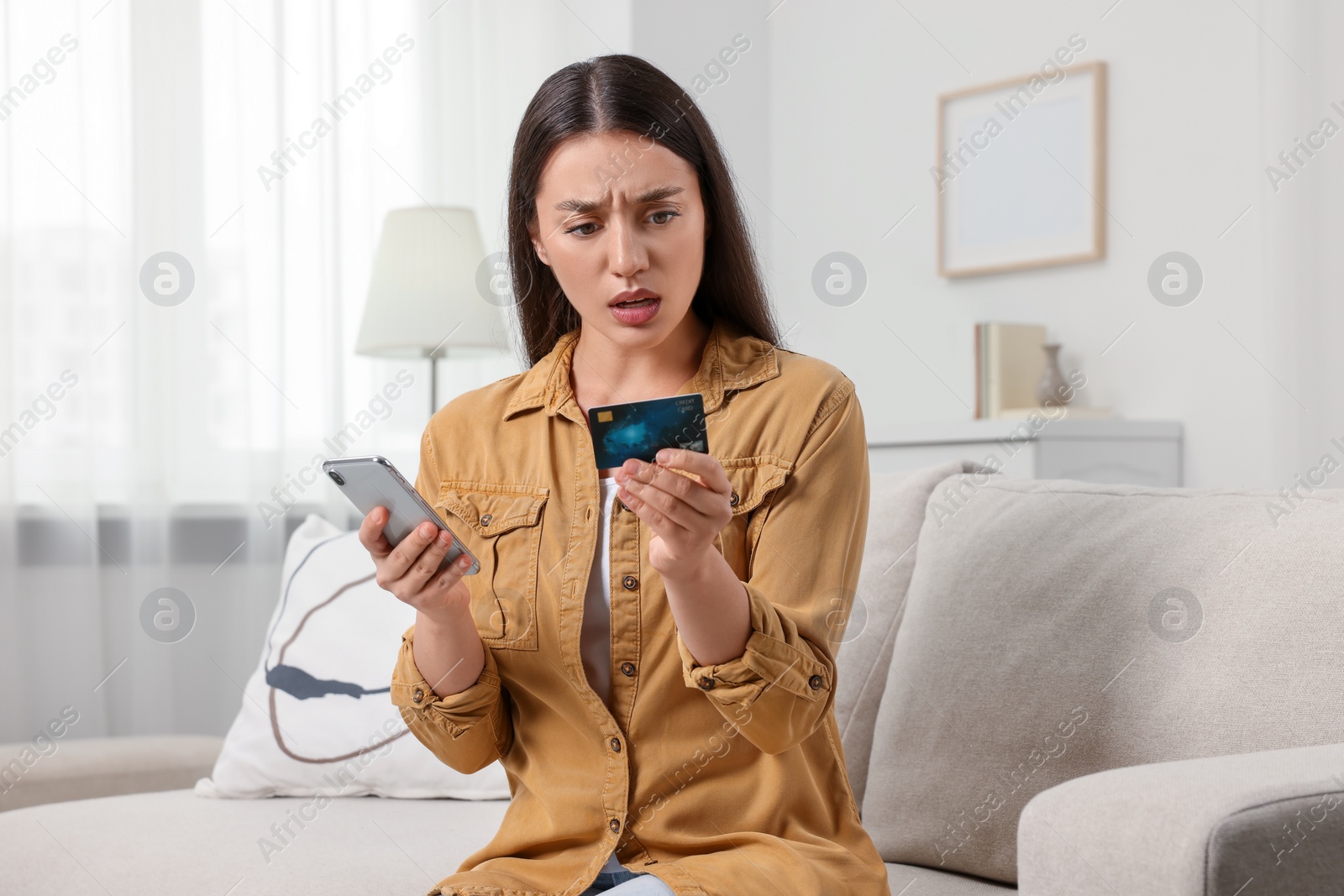 Photo of Shocked woman with credit card and smartphone at home. Be careful - fraud