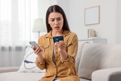 Photo of Shocked woman with credit card and smartphone at home. Be careful - fraud