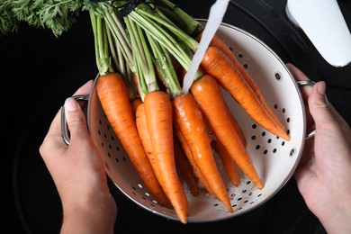 Woman washing ripe carrots in colander with running water over sink, closeup