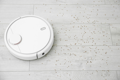 Photo of Removing groats from wooden floor with robotic vacuum cleaner at home. Space for text