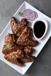 Glazed chicken wings and soy sauce on grey table, top view