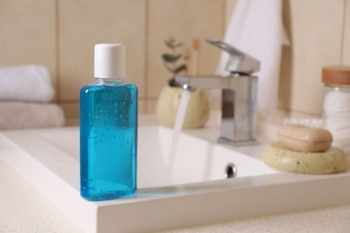 Fresh mouthwash in bottle on sink in bathroom, closeup. Space for text