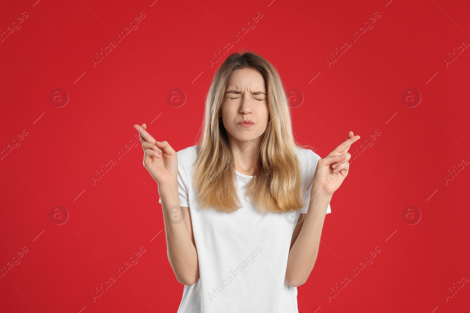 Photo of Woman with crossed fingers on red background. Superstition concept