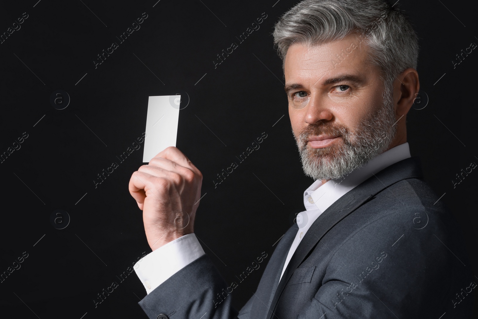 Photo of Handsome businessman holding blank business card on black background