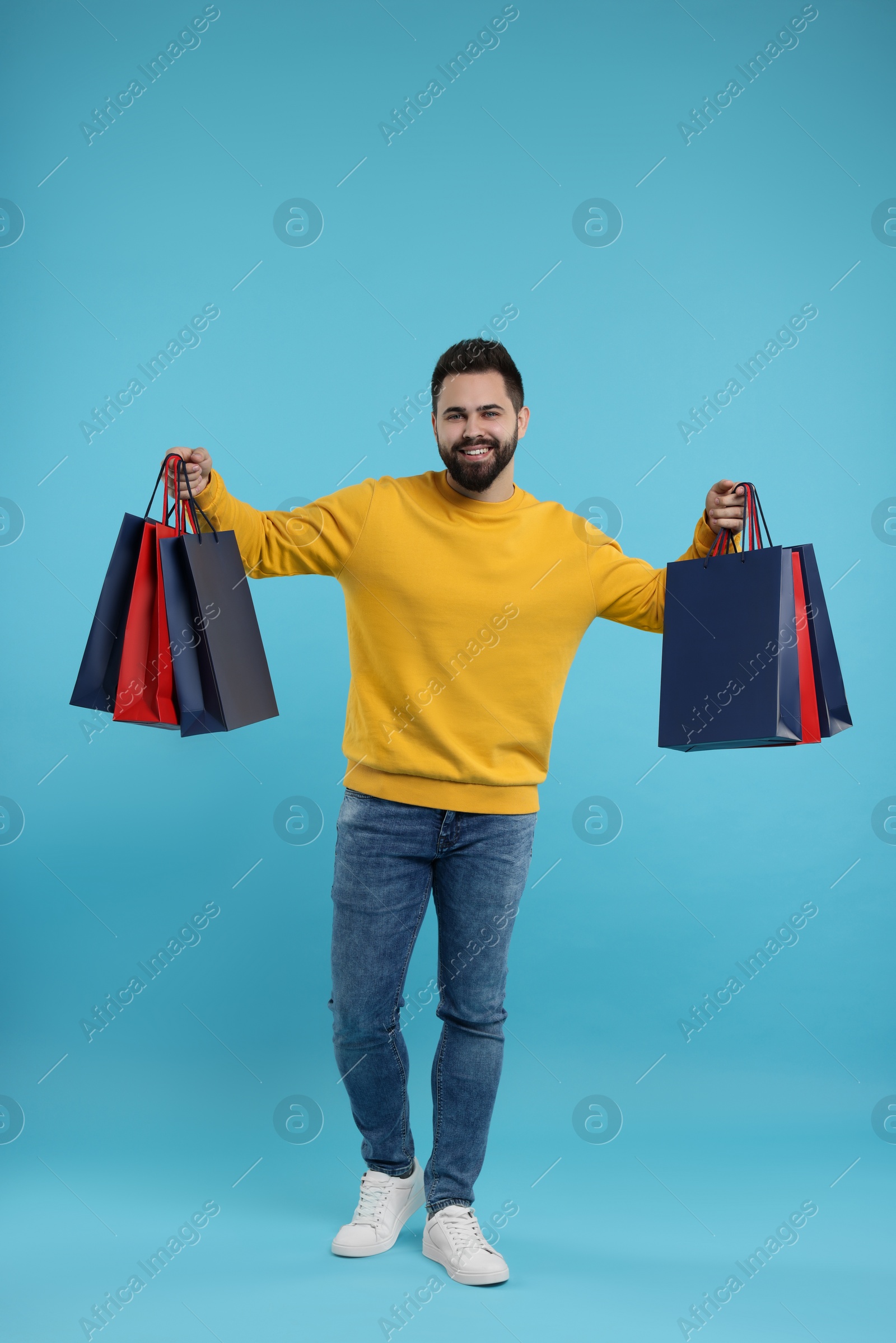 Photo of Smiling man with many paper shopping bags on light blue background