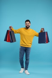 Smiling man with many paper shopping bags on light blue background