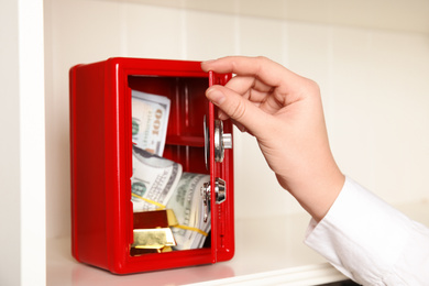 Photo of Woman opening red steel safe on shelf, closeup