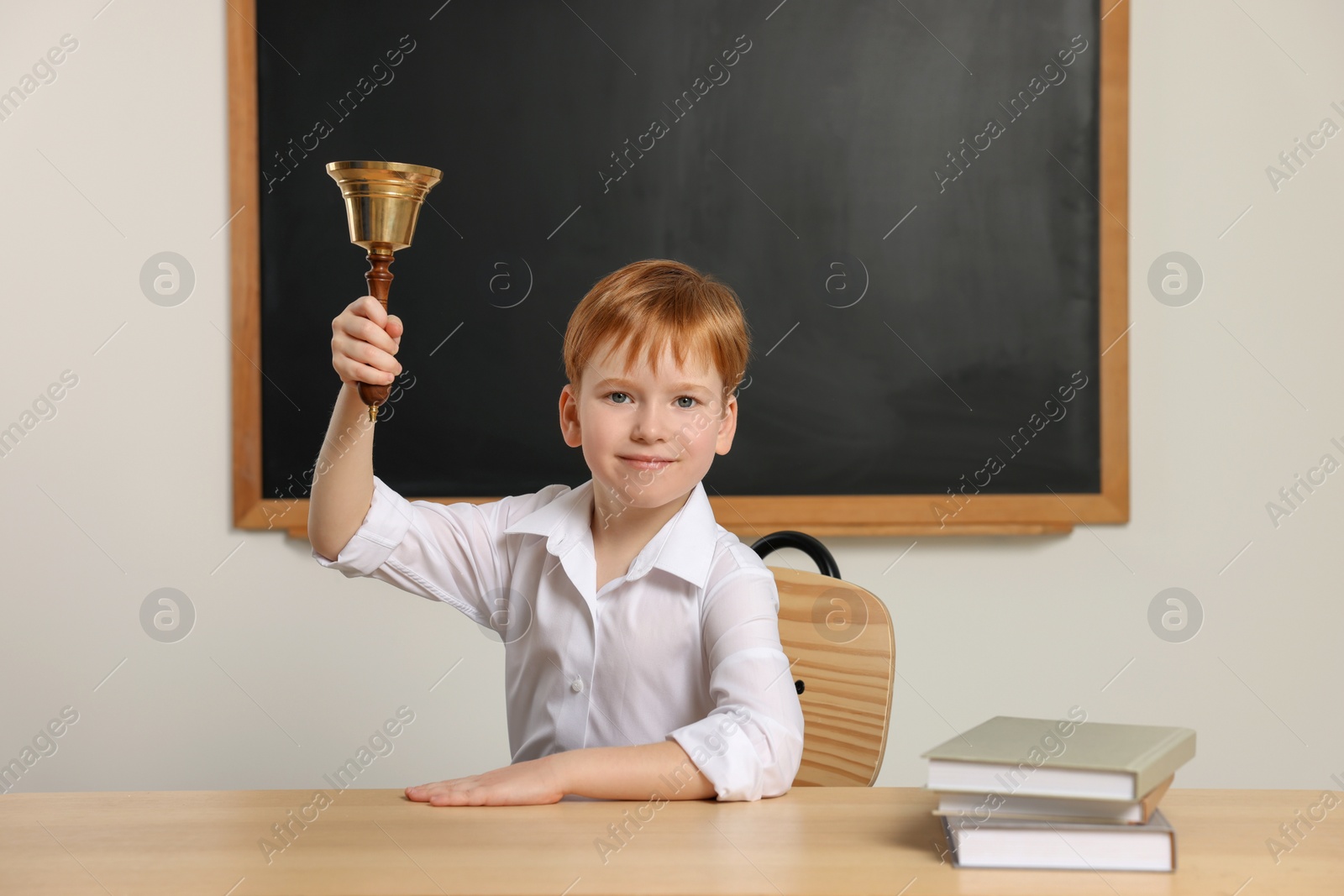 Photo of Cute little boy ringing school bell in classroom