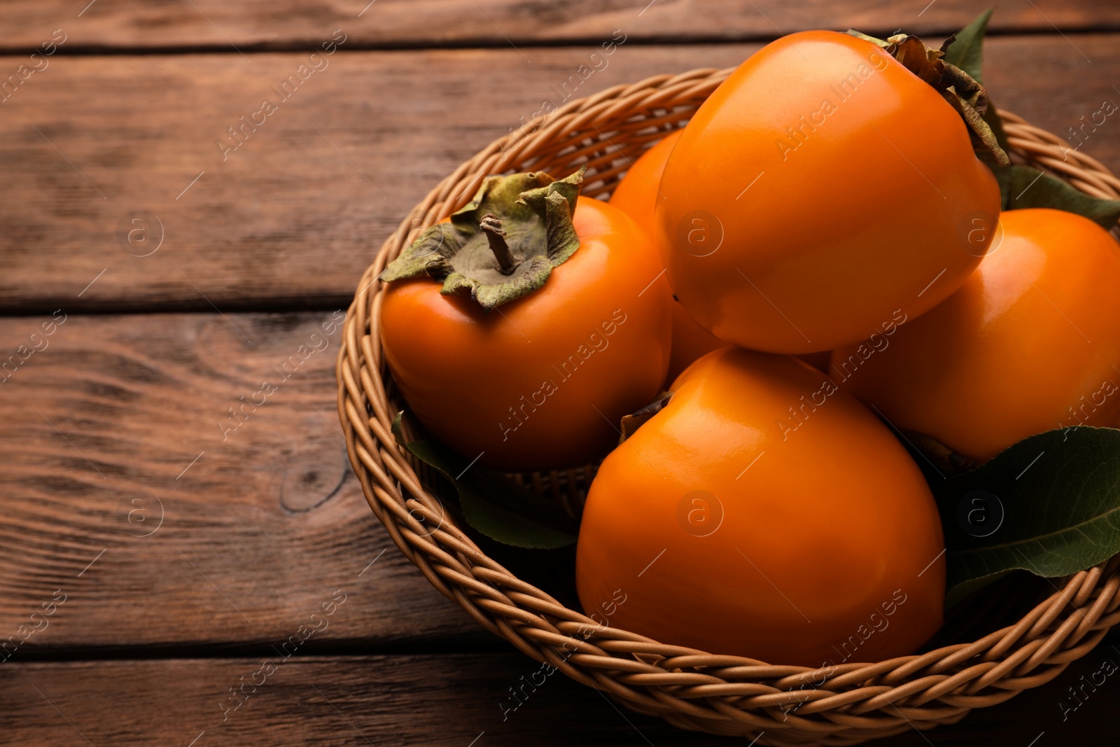 Photo of Delicious ripe persimmons in wicker basket on wooden table
