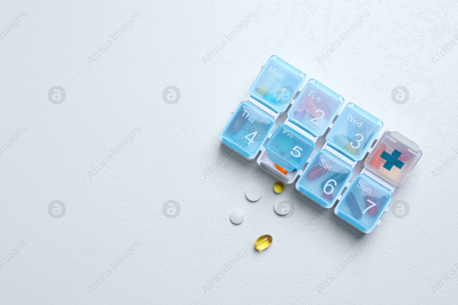 Photo of Weekly pill box with medicaments on white table, flat lay. Space for text