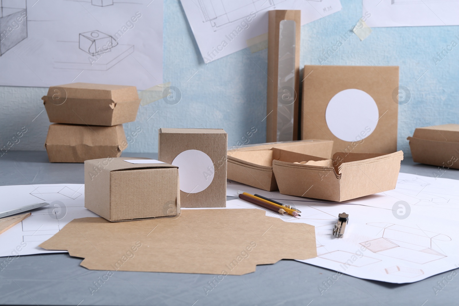 Photo of Creating packaging design. Drawings, boxes and stationery on blue textured table, closeup