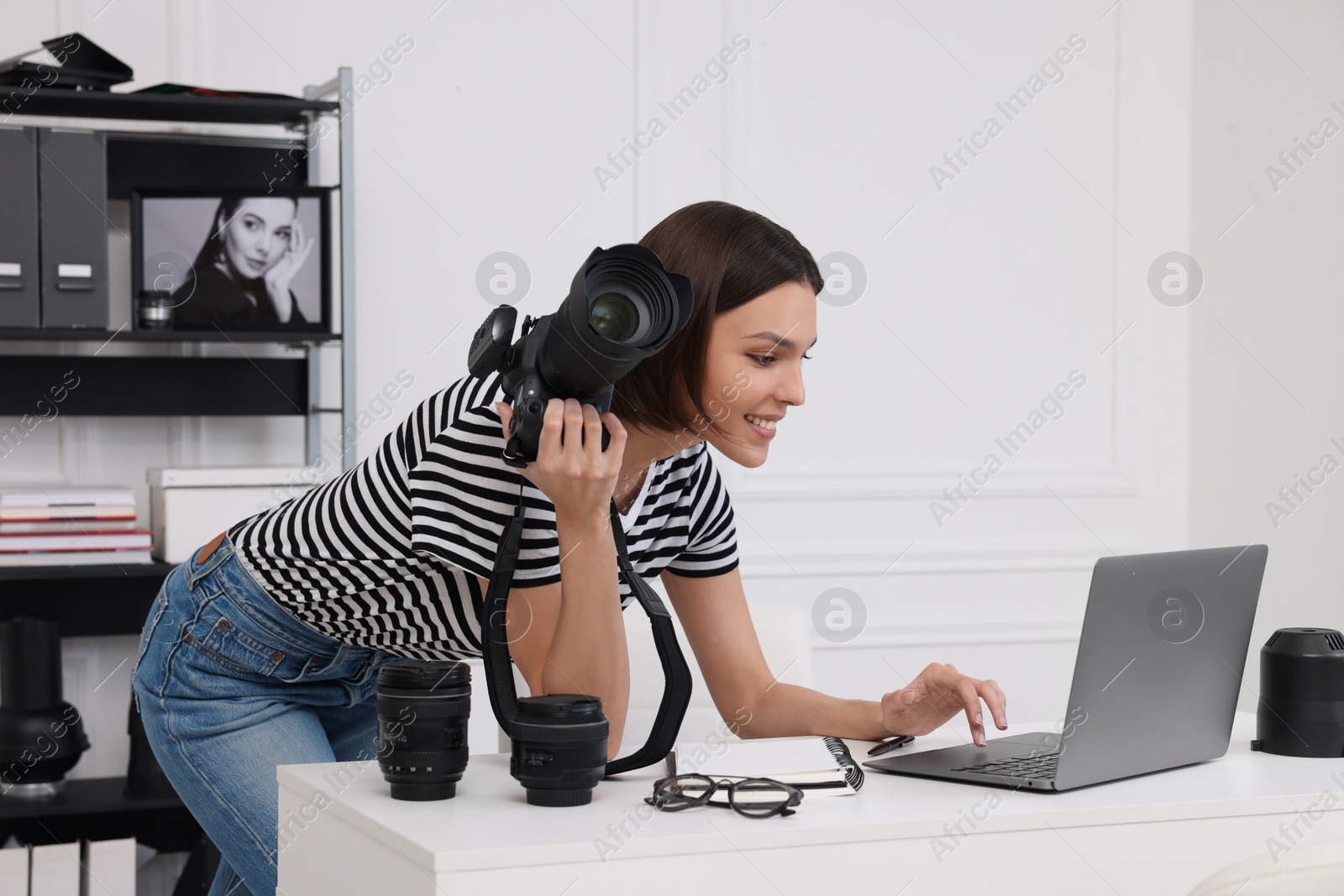 Photo of Young professional photographer with camera working on laptop in modern photo studio