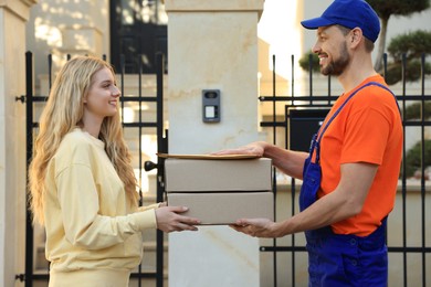 Photo of Woman receiving parcels from courier in uniform outdoors