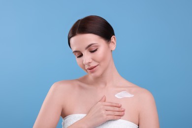 Photo of Beautiful woman with smear of body cream on light blue background