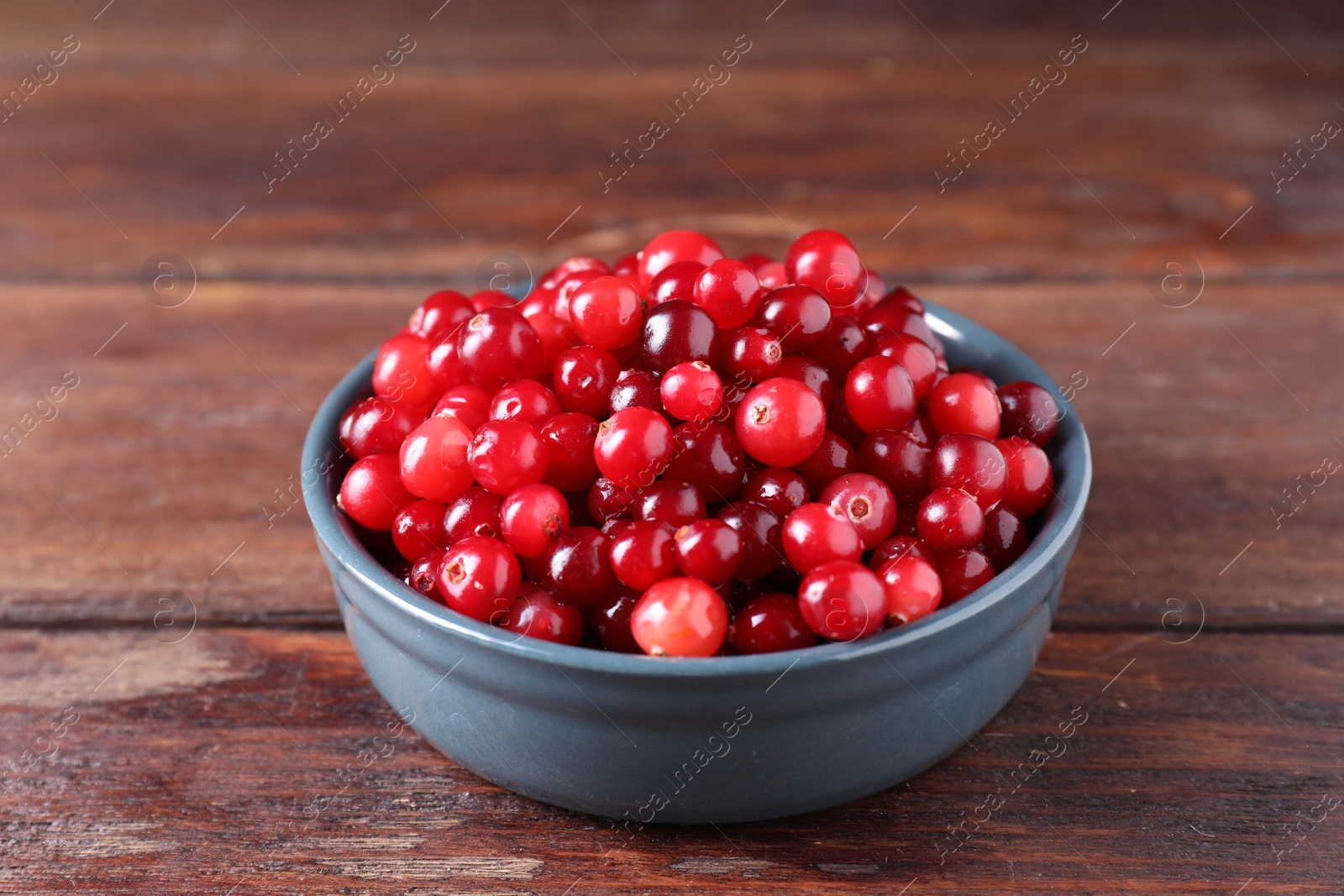 Photo of Fresh ripe cranberries in bowl on wooden table, closeup