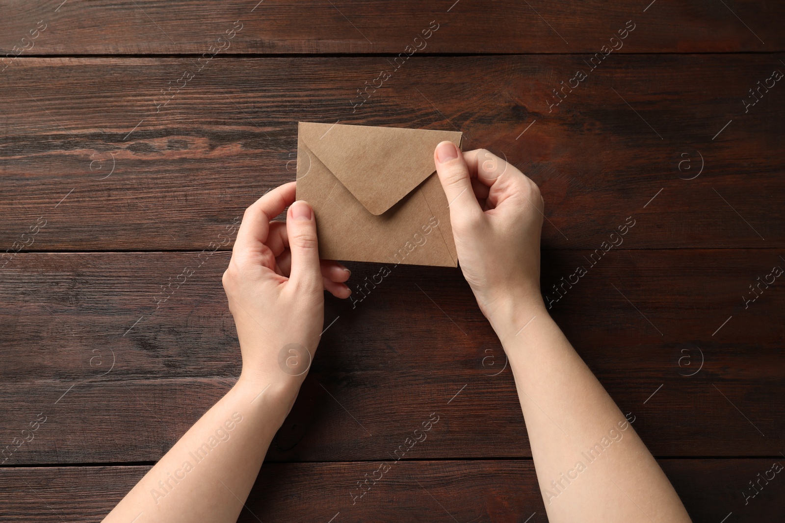 Photo of Woman with kraft paper envelope at wooden table, top view