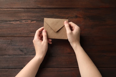 Woman with kraft paper envelope at wooden table, top view