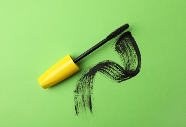 Photo of Mascara wand and smear on green background, top view. Makeup product