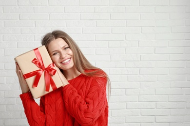 Photo of Happy young woman with Christmas gift near white brick wall. Space for text