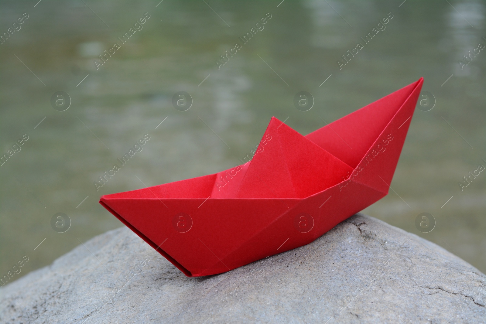 Photo of Beautiful red paper boat on stone outdoors, closeup