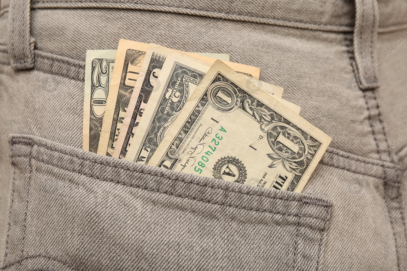 Photo of Dollar banknotes in pocket of grey jeans, closeup. Spending money