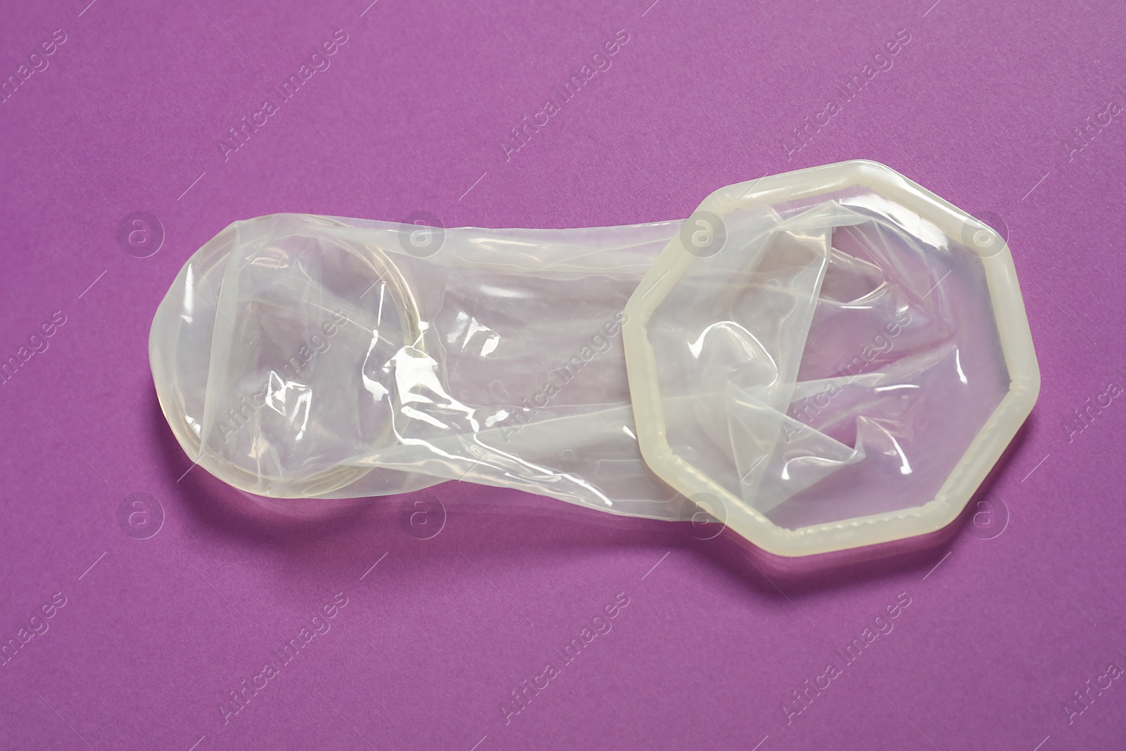 Photo of Unrolled female condom on violet background, closeup. Safe sex