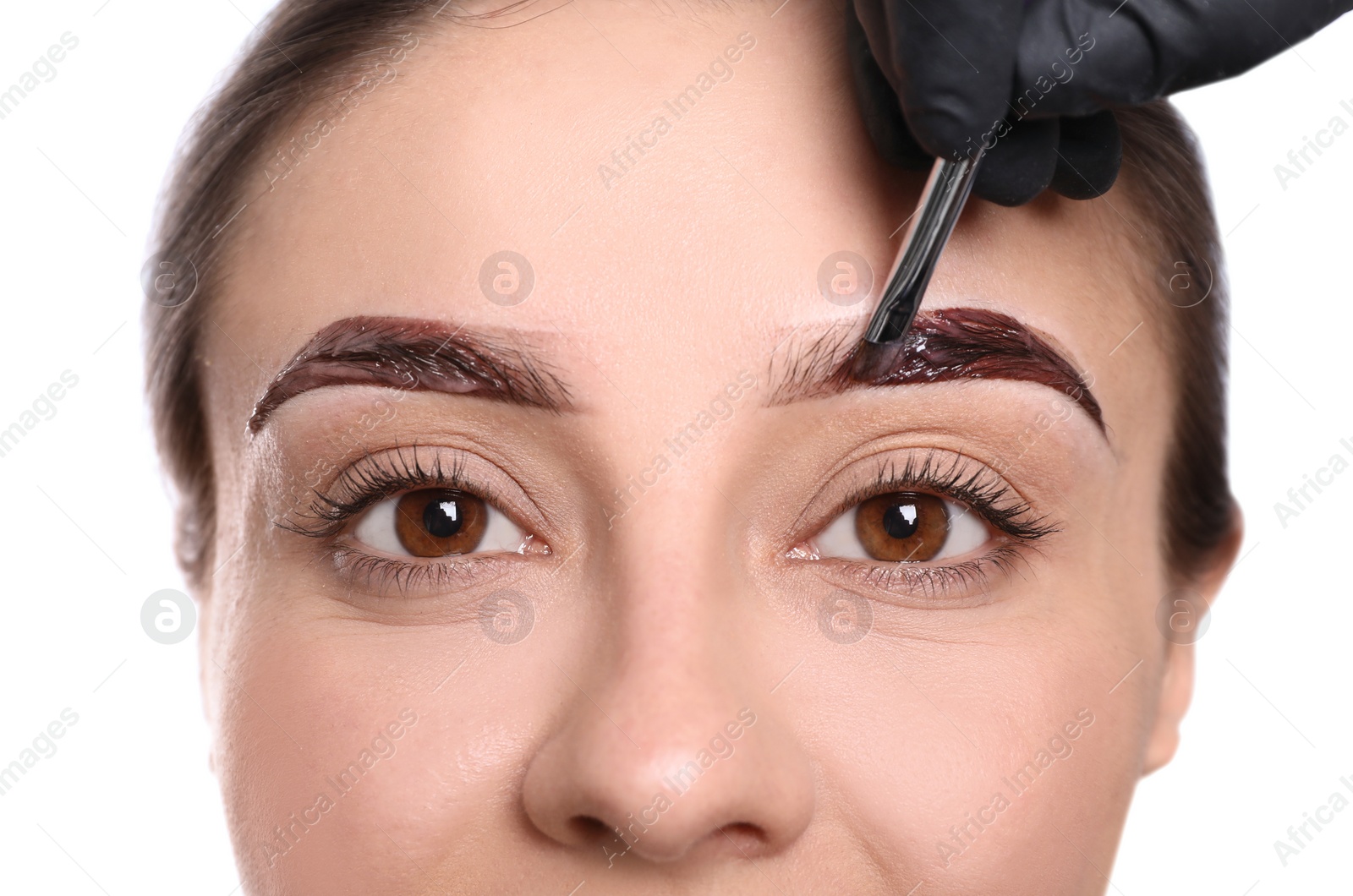 Photo of Beautician applying tint during eyebrows correction procedure on white background, closeup