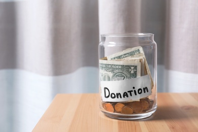 Glass jar with money and label DONATION on table against blurred background. Space for text