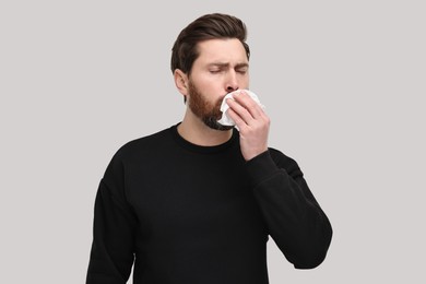 Sick man with tissue coughing on light grey background