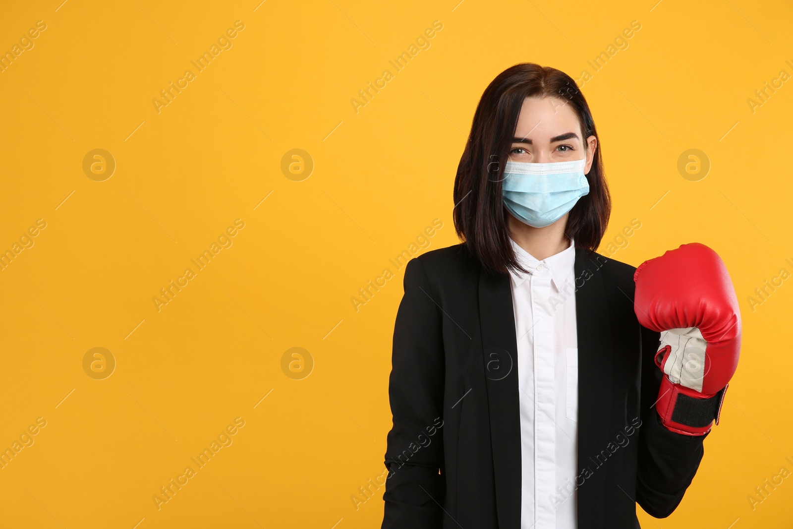 Photo of Businesswoman with protective mask and boxing gloves on yellow background, space for text. Strong immunity concept