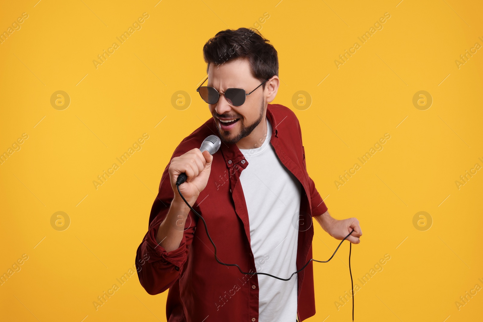 Photo of Handsome man with sunglasses and microphone singing on yellow background