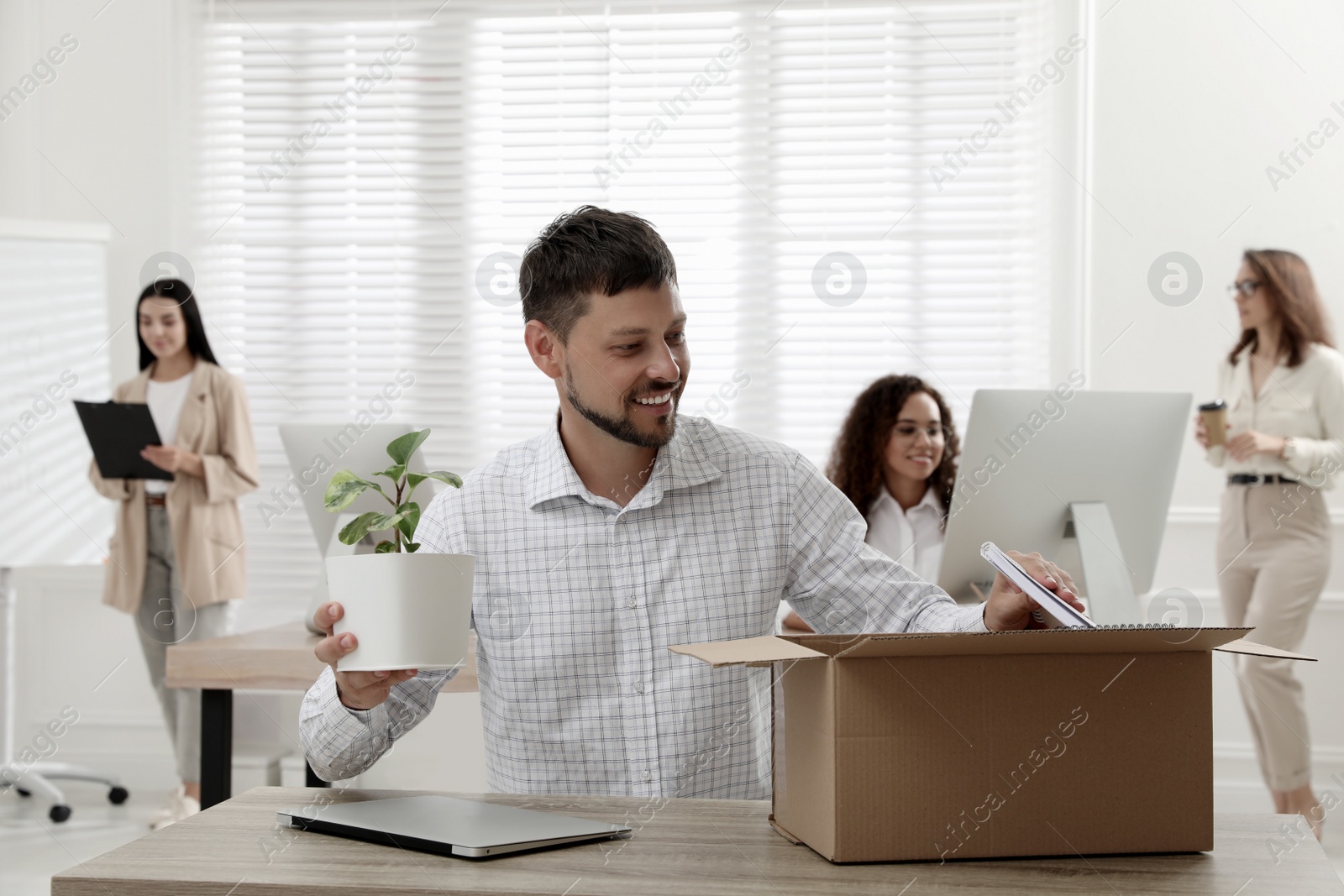 Photo of New coworker unpacking box with personal items at workplace in office