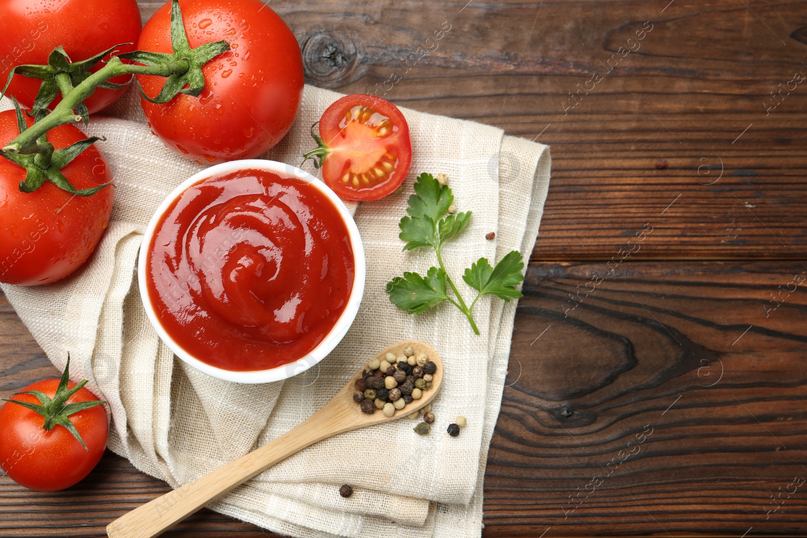 Photo of Delicious ketchup in bowl, tomatoes, parsley and peppercorns on wooden table, top view. Space for text