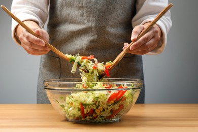 Photo of Woman making tasty salad with Chinese cabbage at wooden table, closeup