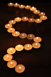 Photo of Burning candles on wooden table in darkness