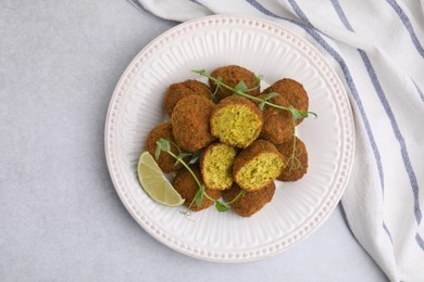 Photo of Delicious falafel balls, lime slice and microgreens on light table, top view