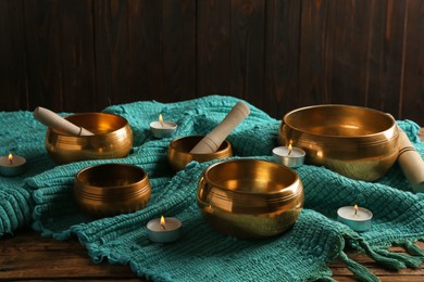 Photo of Tibetan singing bowls with mallets, burning candles and turquoise fabric on wooden table