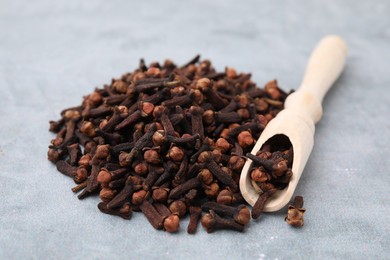 Photo of Pile of aromatic dried clove buds and scoop on grey table, closeup