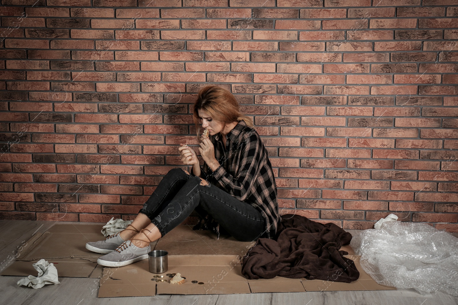 Photo of Poor homeless woman eating on floor near brick wall