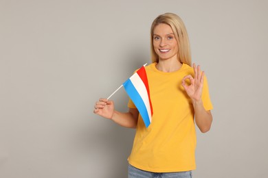 Photo of Woman with flag of Netherlands showing ok gesture on light grey background, space for text