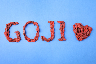 Photo of Word GOJI and heart made of dried berries on blue background, flat lay