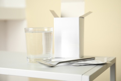 Medicine sachets, glass of water and spoon on white table