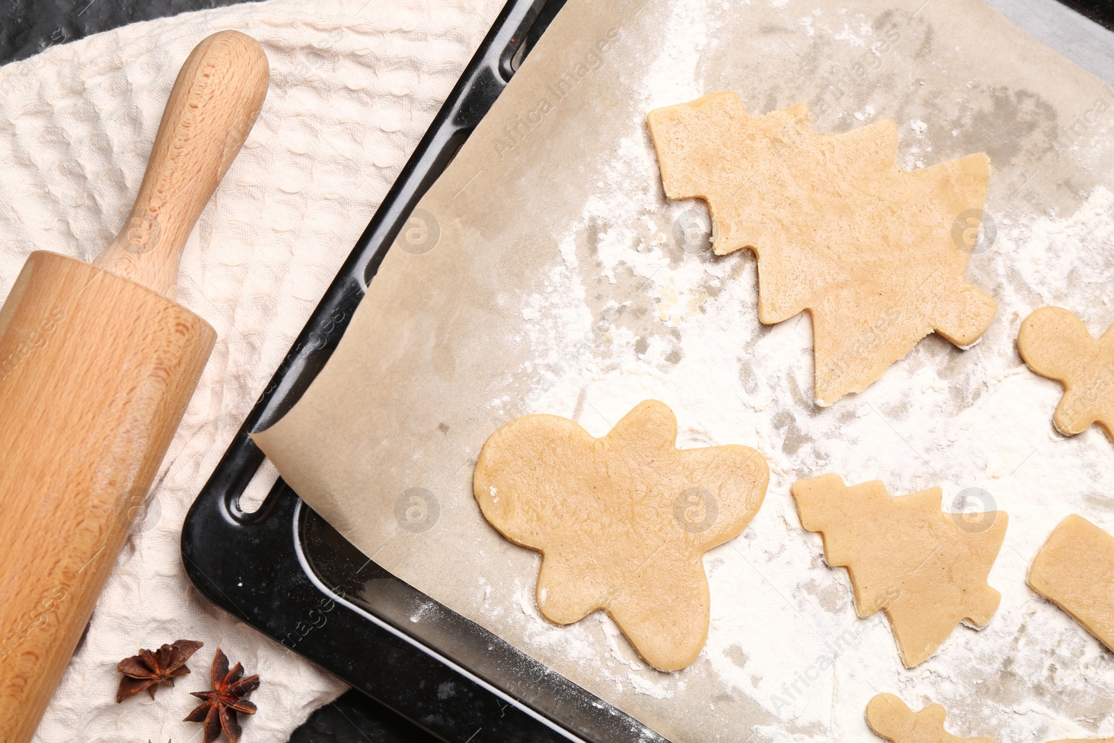 Photo of Raw Christmas cookies in baking tray, rolling pin and anise stars on table, flat lay