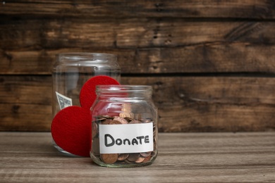 Photo of Donation jars with money and red heart on table. Space for text