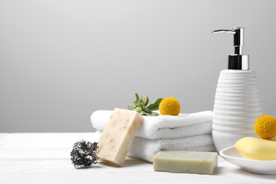 Soap bars, bottle dispenser and towels on wooden table against white background, space for text